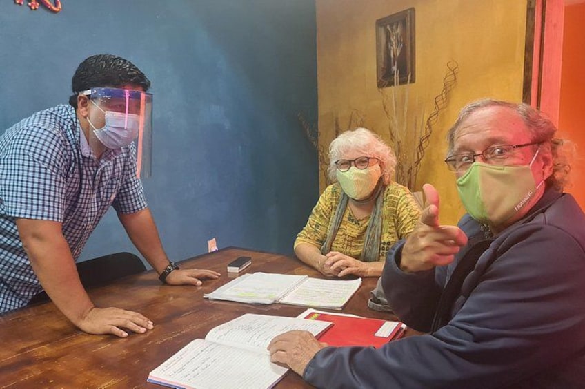 Three people sitting at a wooden table with documents, one person wearing a face shield. 2