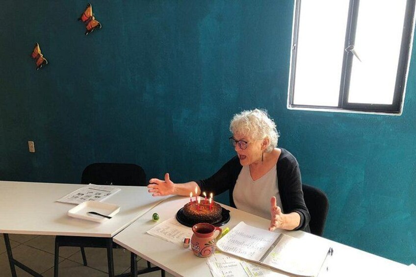 A person sitting at a table with a cake and candles, surrounded by papers and a cup. 5