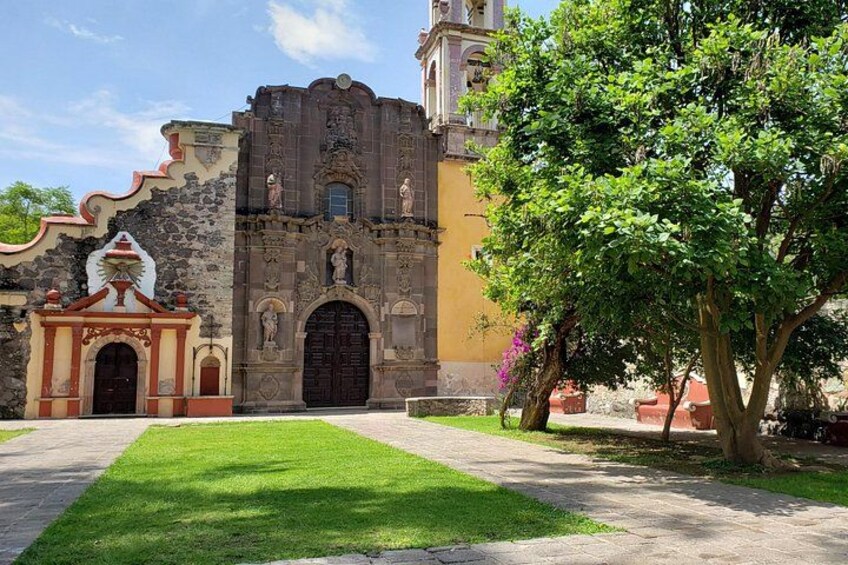 A historic building with a large arched doorway, a bell tower, and a small shrine. 3