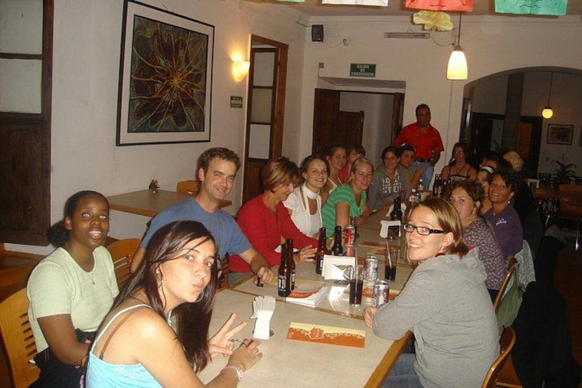 A group of people sitting around a table in a restaurant with a large painting on the wall. 4