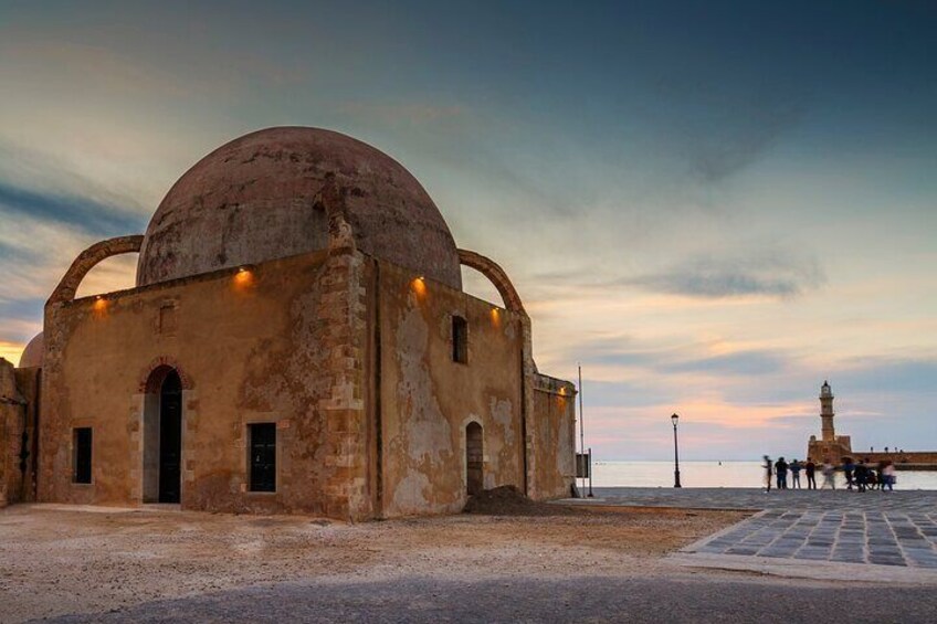 Un edificio antiguo con una cúpula y ventanas de arco, una zona pavimentada y un faro distante. 5