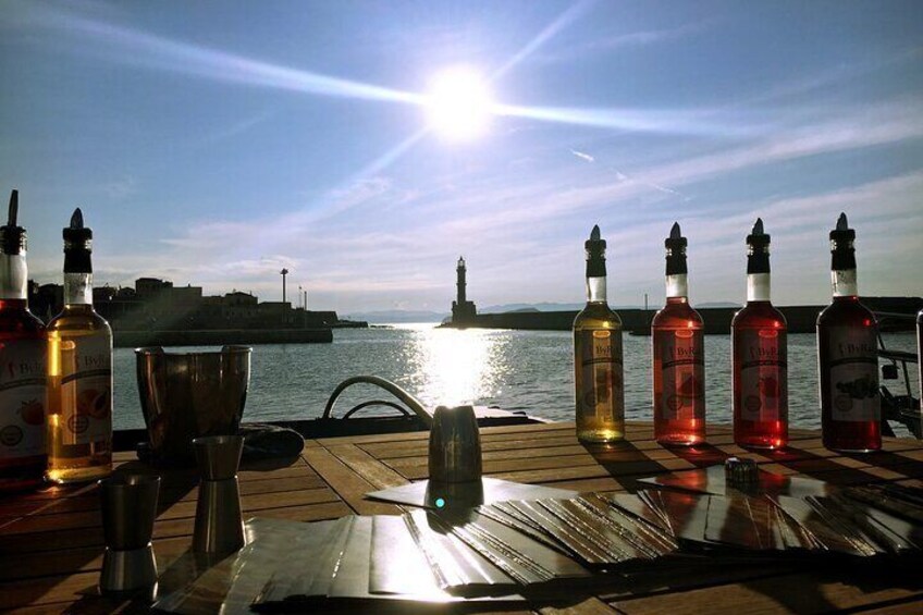 Botellas de licores sobre una mesa de madera, con vista a un cuerpo de agua y un horizonte urbano distante. 2