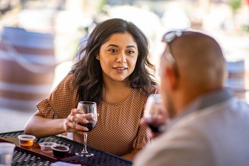 Une personne assise à une table avec un verre de vin, une autre personne partiellement visible, et un menu. 3