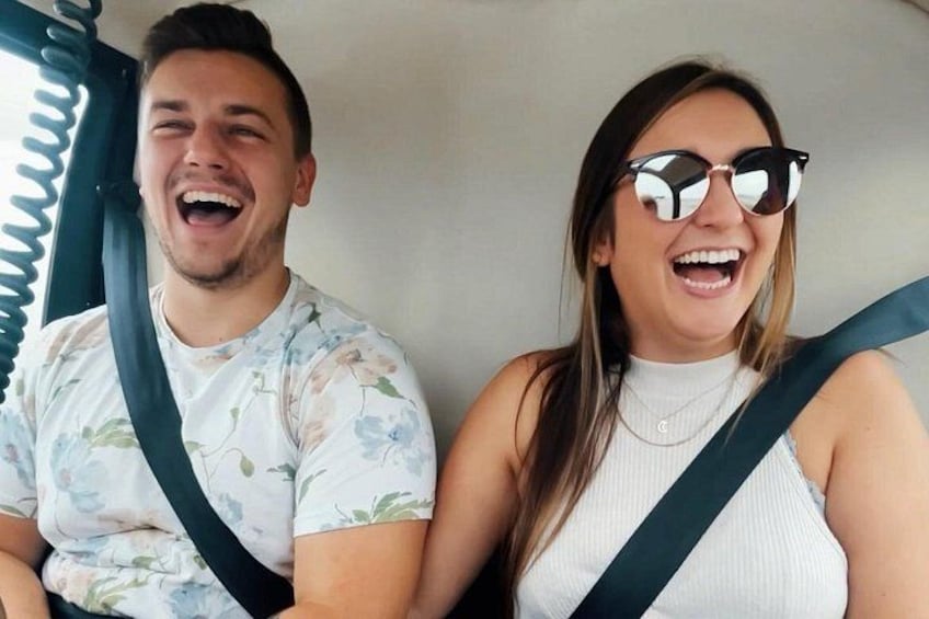 Two people in a vehicle with a floral pattern on the man's shirt and a white top on the woman. 5