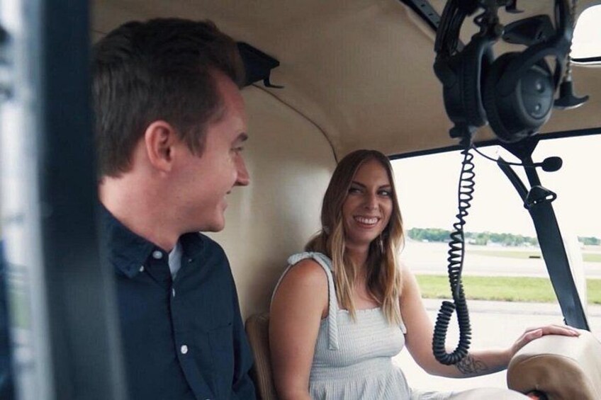 A man and a woman in a vehicle, with a seatbelt visible and a landscape outside. 2