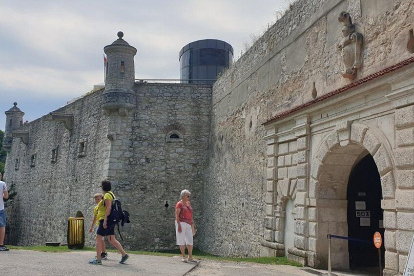 A historic stone wall with a gate, a person walking, and a clear sky. 2