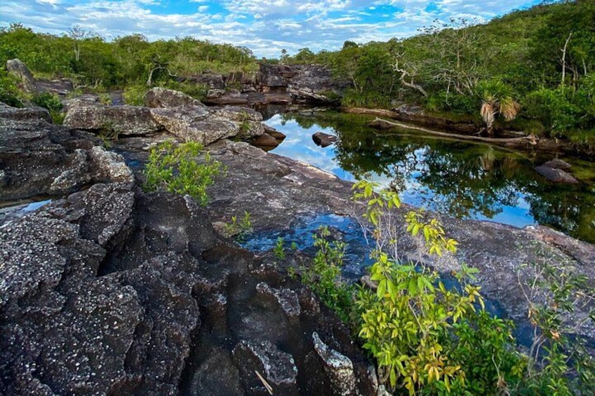 A rocky landscape with a calm water body, surrounded by greenery and trees. 2