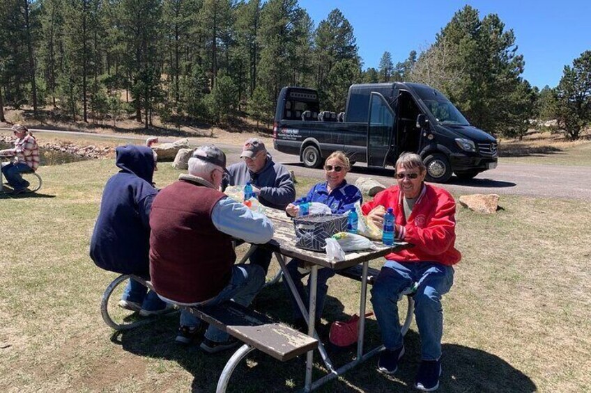 A group of people sitting at a table outdoors with a vehicle in the background. 5