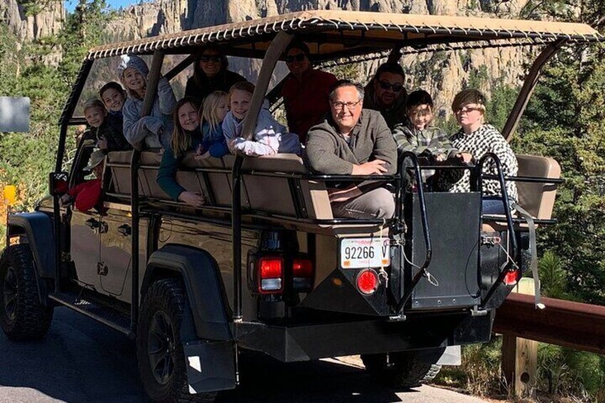 A group of people in a safari vehicle on a road with a mountainous backdrop. 3