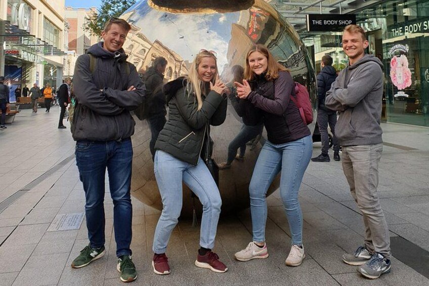 Un grupo de personas posando frente a una escultura grande y reflectante en un entorno urbano. 4