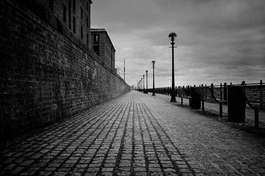 A cobblestone pathway, brick wall, and benches along a waterfront. 5