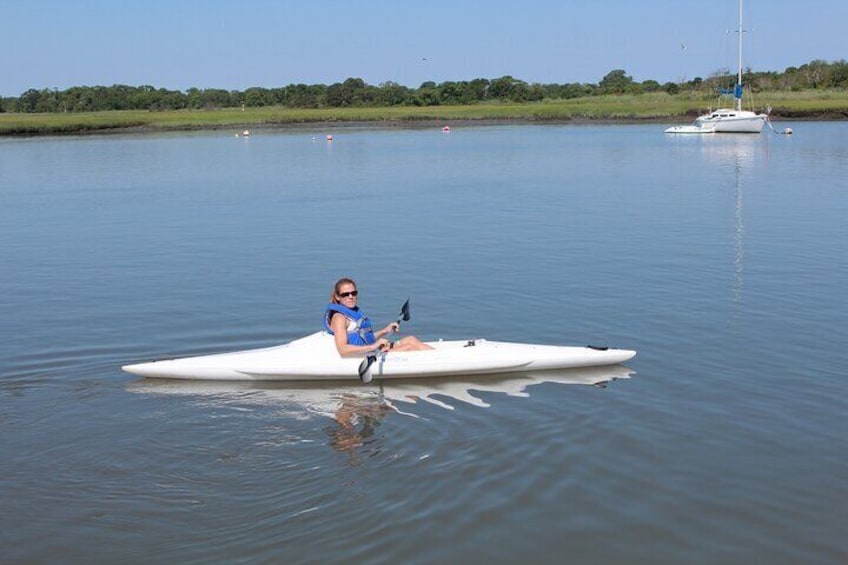 A person kayaking on a calm body of water with a sailboat in the background. 5