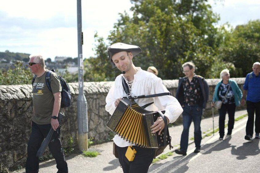 A person playing a traditional accordion on a stone wall, with pedestrians in the background. 3