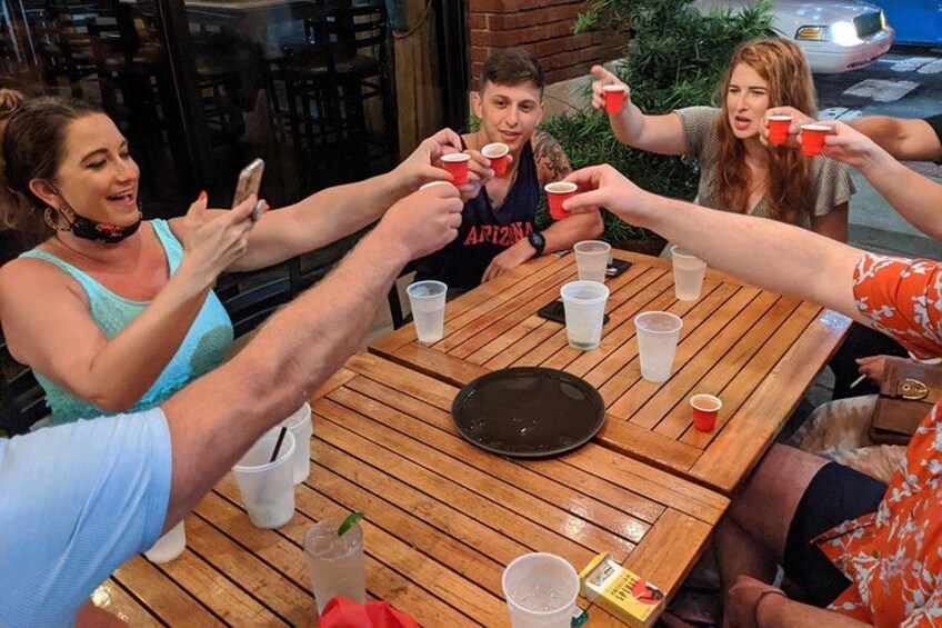 A group of people toasting with red cups around a wooden table with a black plate and a glass of a beverage. 5
