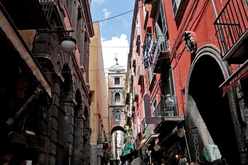 A narrow street with red buildings, a church with a dome, and a large archway. 1