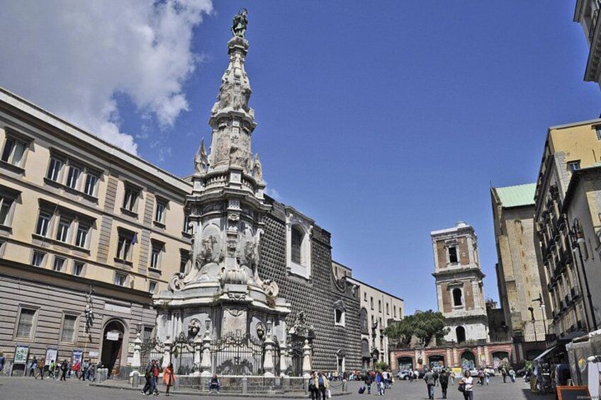 A historic plaza with ornate sculptures, a prominent church tower, and classical architecture. 5