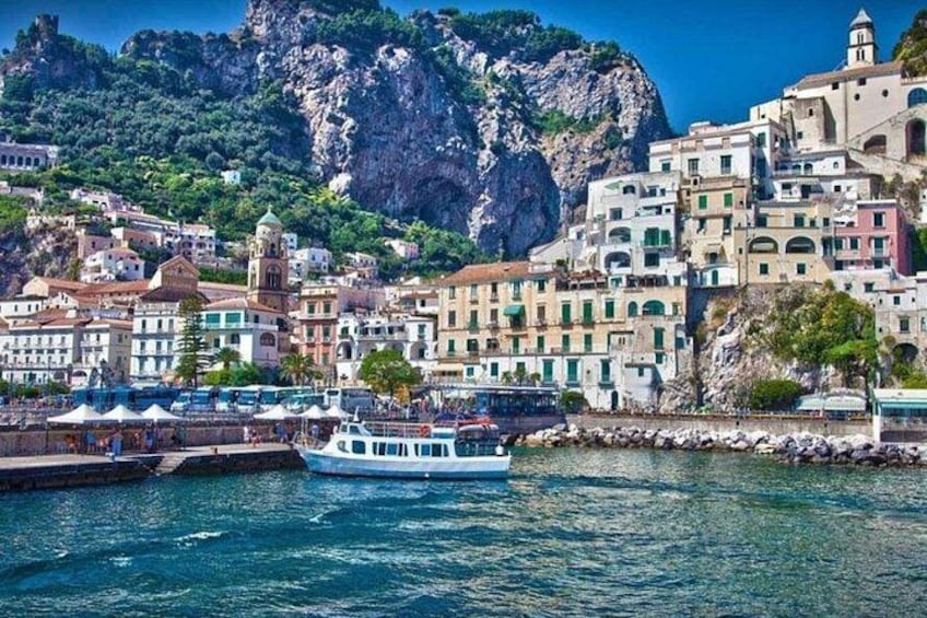 A coastal town with colorful buildings, a boat docked at the pier, and a rocky mountain in the background. 1