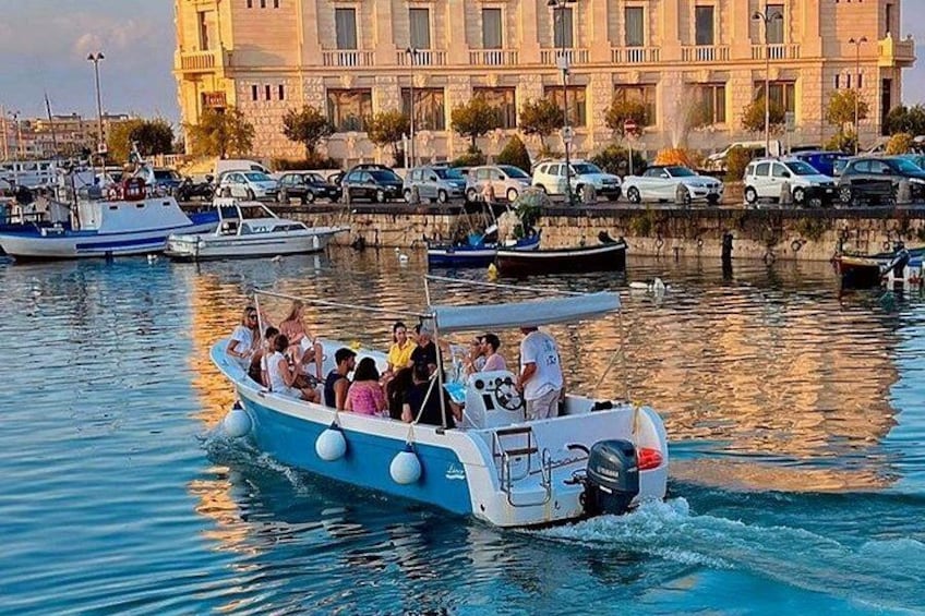 A blue boat with passengers, docked near a building with a port in the background. 3