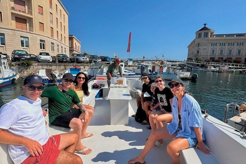 A group of people on a boat in a marina with buildings and parked cars in the background. 3
