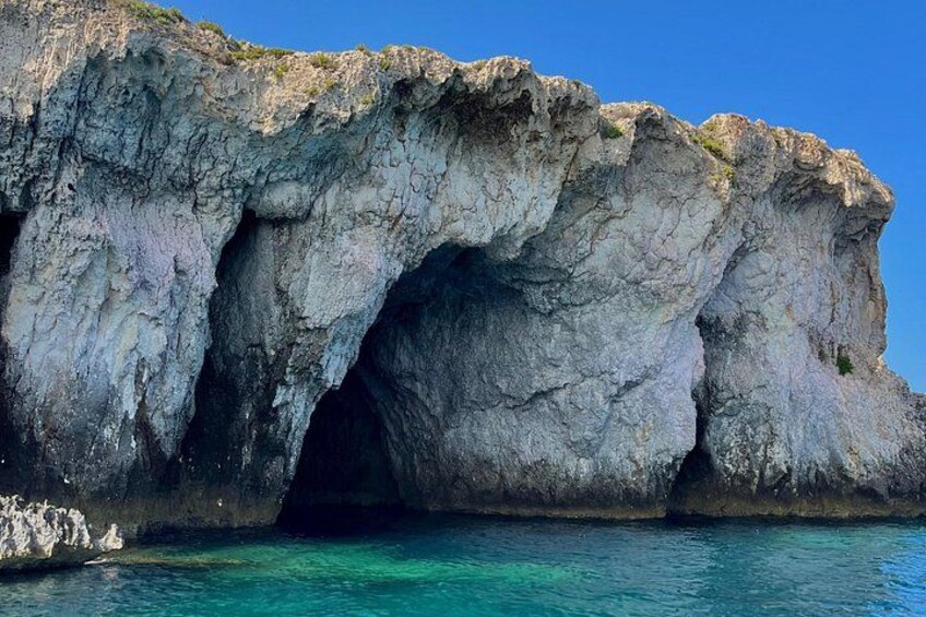 A large rock formation with a cave entrance and clear blue water. 2