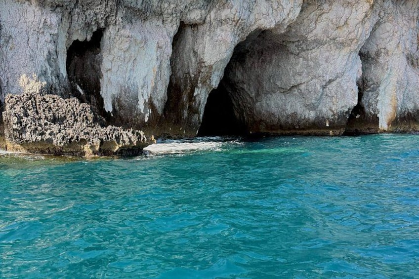A rocky coastline with a cave entrance and clear blue waters. 5