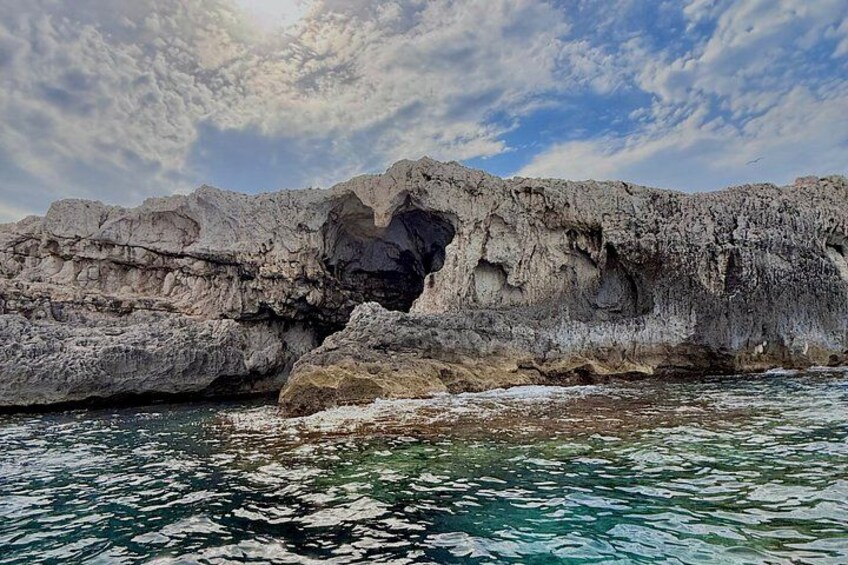 A rocky coastline with a large cave-like formation and clear turquoise water. 1