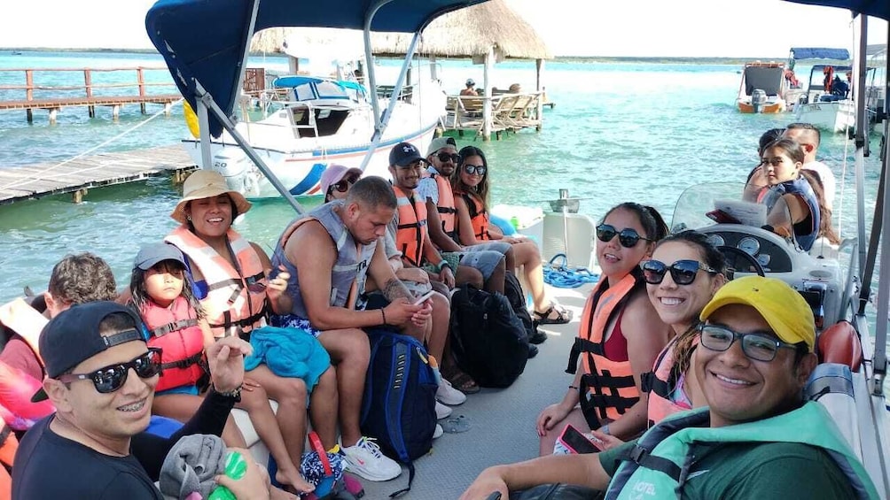 A group of people on a boat, wearing life jackets, with a thatched-roof structure in the background. 1