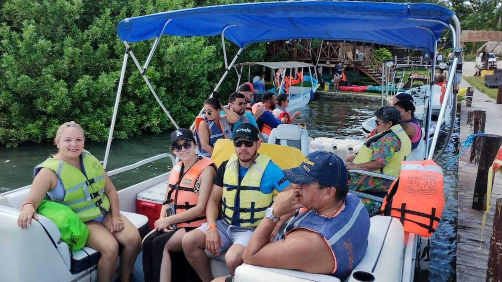 A group of people on a boat with life jackets, surrounded by water and greenery. 3