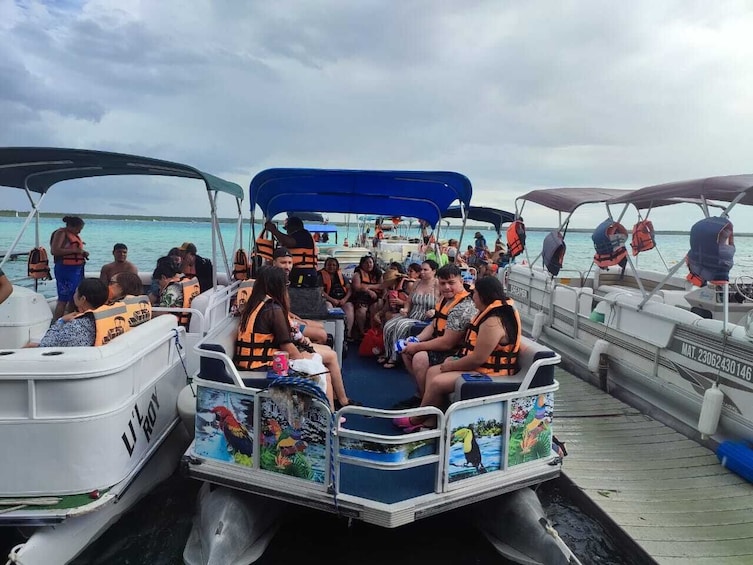 A group of people on a boat with life jackets, a dock, and calm water. 4