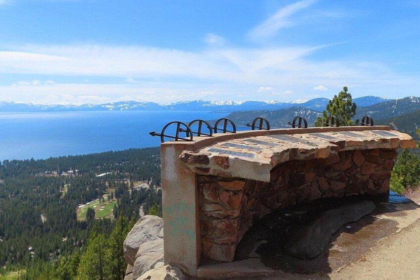 Un banc en pierre, agrémenté de garde-corps en métal, offre une vue sur un paysage montagneux avec un lac. 3