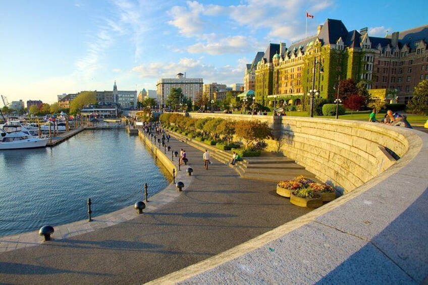 A waterfront promenade with a curved stone wall, a marina with boats, and a large building with a flag. 2