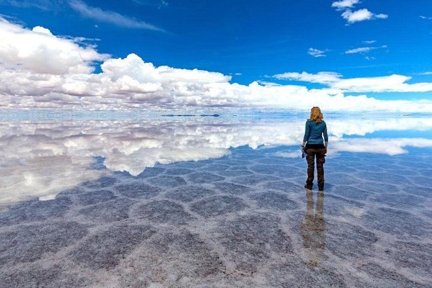 A person standing on a reflective salt flat with clouds in the sky. 4