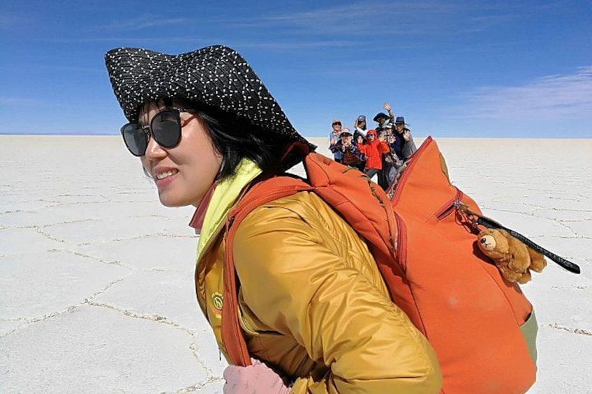 A person in a yellow jacket and black hat with a large orange backpack, standing in a vast white landscape. 1