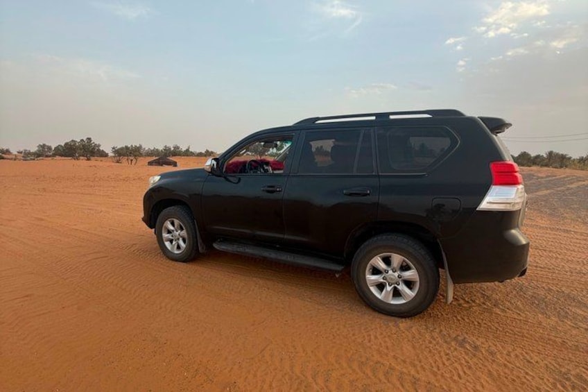 A black SUV parked on a sandy terrain with sparse vegetation in the background. 4