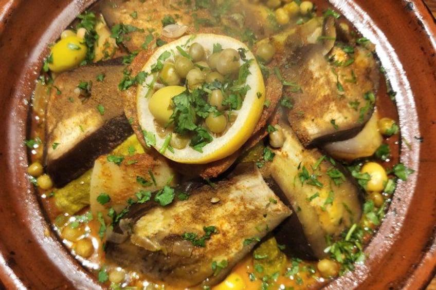 A traditional stew with fish, potatoes, and garnishes like parsley and olives in a clay pot. 3