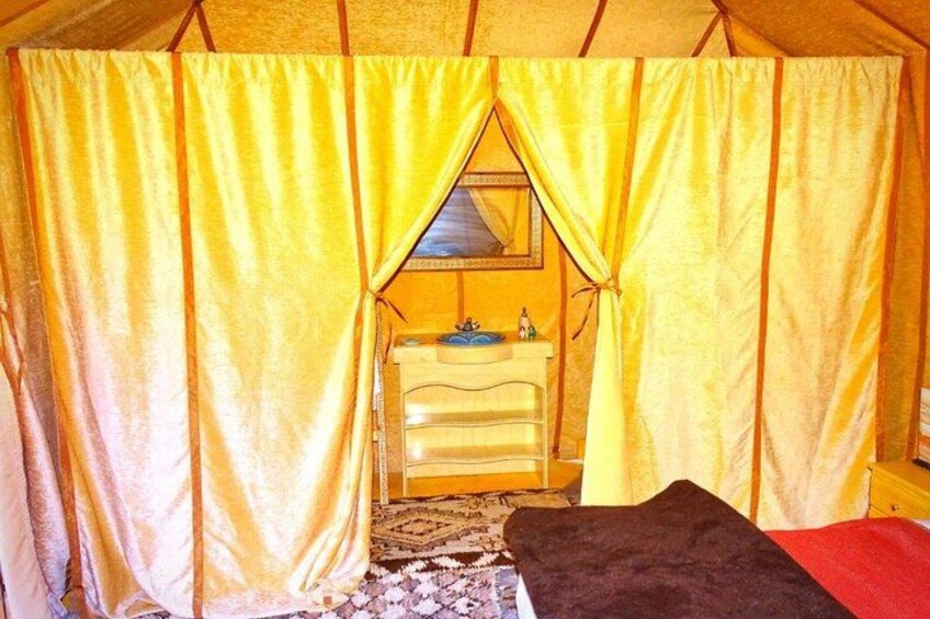 A tent interior with yellow curtains, a white dresser, and a black blanket. 4