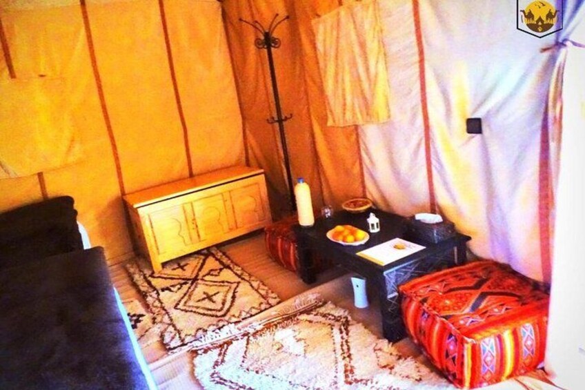 A tent interior with a wooden chest, a table with a bottle, a bowl, and a red patterned cushion. 3