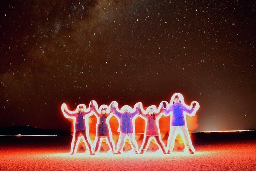 A group of people holding hands in a line, illuminated by a neon light against a night sky. 3