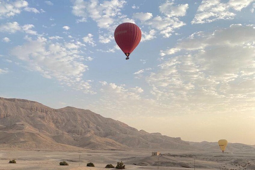 Un paysage désertique avec des montagnes en arrière-plan et deux montgolfières dans le ciel, une rouge et une jaune. 4