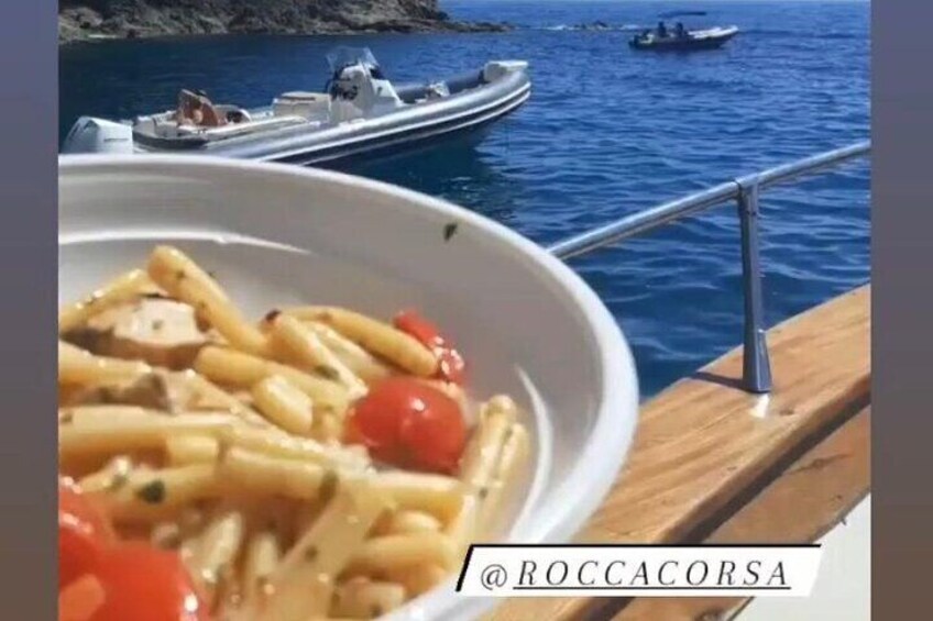 A bowl of pasta with cherry tomatoes on a boat deck with boats in the background. 4