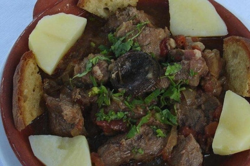 A stew with chunks of meat, potatoes, and herbs in a ceramic dish. 5