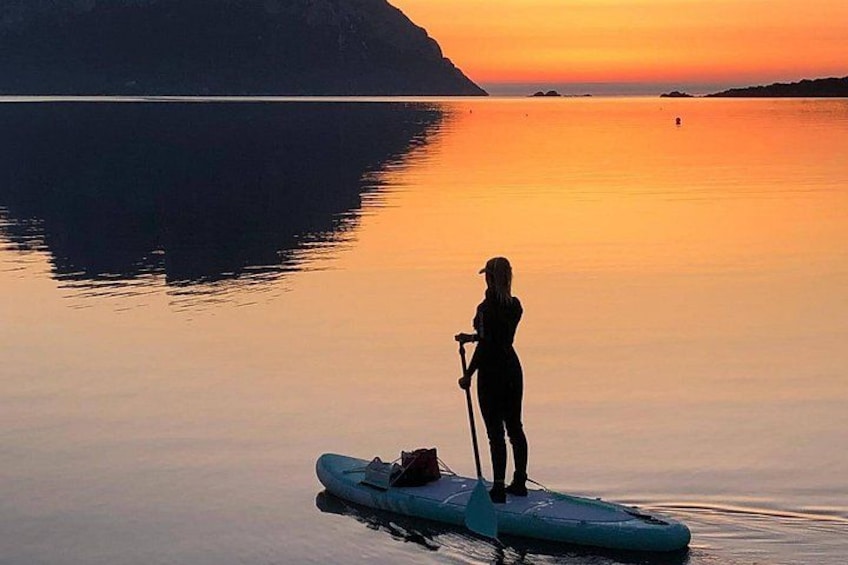 Una persona haciendo paddleboard sobre aguas tranquilas al atardecer, con una montaña de fondo. 4