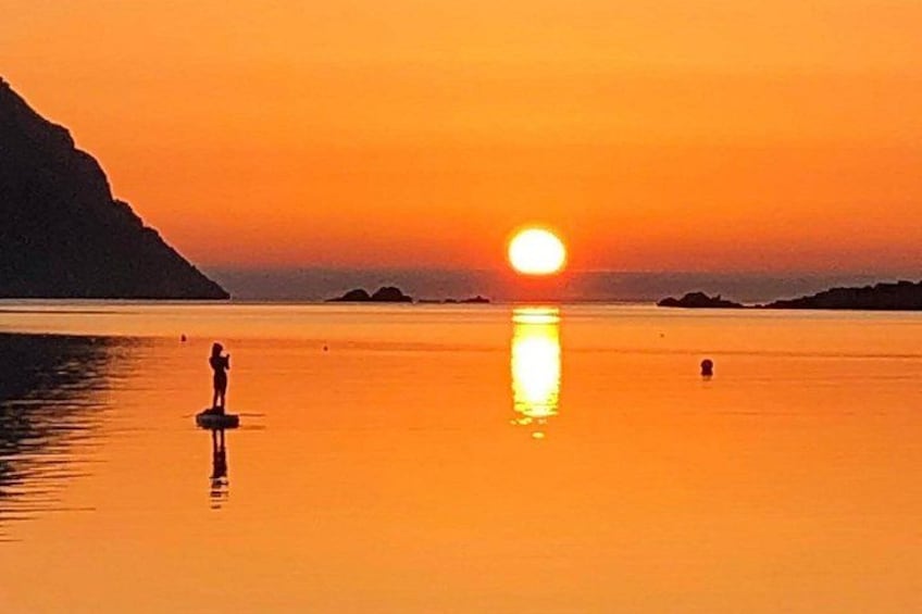 Un atardecer sobre una superficie acuática tranquila con una persona de pie en una plataforma flotante. 3
