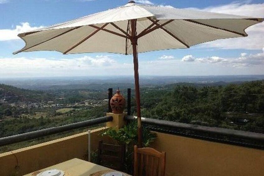 A balcony with a table, chairs, and a large umbrella overlooking a scenic landscape. 2