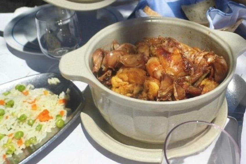 A meal with a pot of chicken, a side of rice with peas, and a glass of water. 2