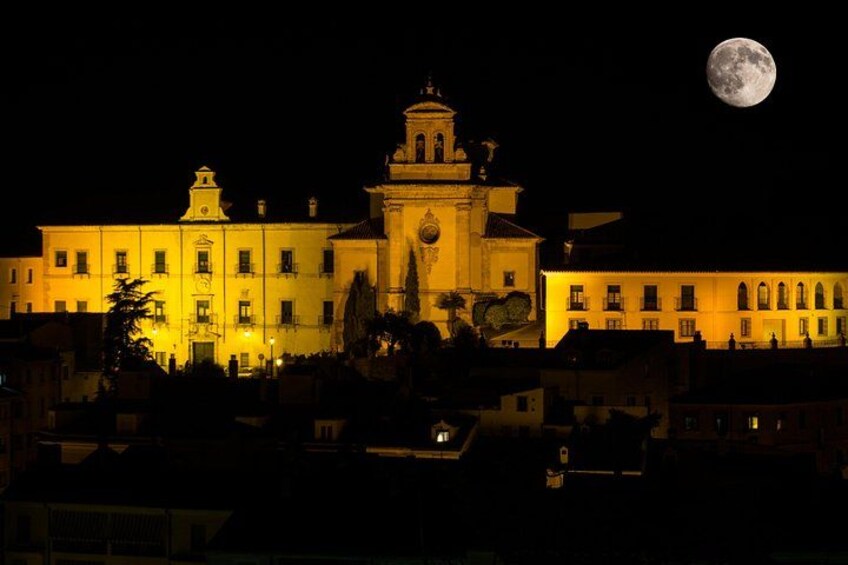 A large illuminated building with a prominent tower, a full moon in the sky, and surrounding urban structures. 2