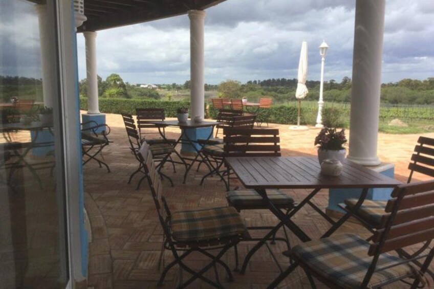 Une terrasse extérieure avec des tables et des chaises en bois, des colonnes blanches et une vue sur un vignoble. 2