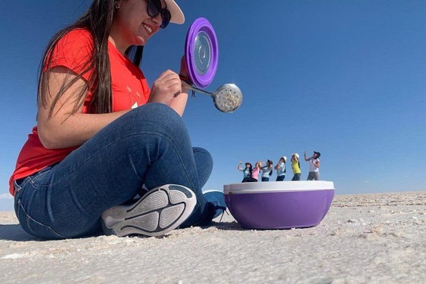 Una persona sentada en el suelo sosteniendo una pesa púrpura, con un grupo de personas de pie sobre una plataforma elevada al fondo. 4