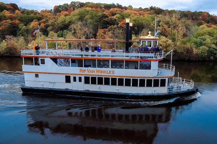 A white riverboat named 'Rip Van Winkle' with a cabin and a flag, sailing on a river with autumn trees in the background. 1