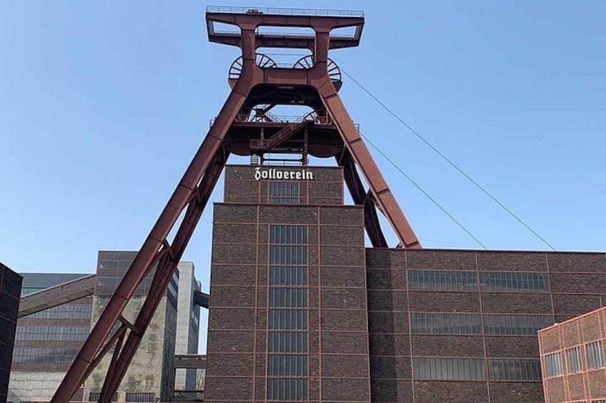 A tall, red metal structure with the word 'Göloerein' on it, surrounded by modern buildings. 3